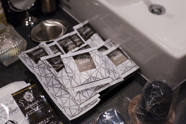 Una encimera de baño con distintos artículos de aseo y una botella de fragancia corporal AROMADOR.