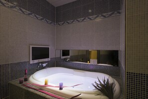 Un baño con una bañera grande, un espejo sobre el lavamanos y paredes con azulejos.