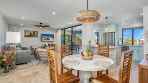 A modern living room with a dining area, featuring a round table with chairs, a sofa, and a ceiling fan.