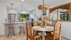 A modern kitchen with a central island, bar stools, and a dining table set with a fruit bowl.