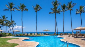 A pool area with palm trees, lounge chairs, and a view of the ocean.