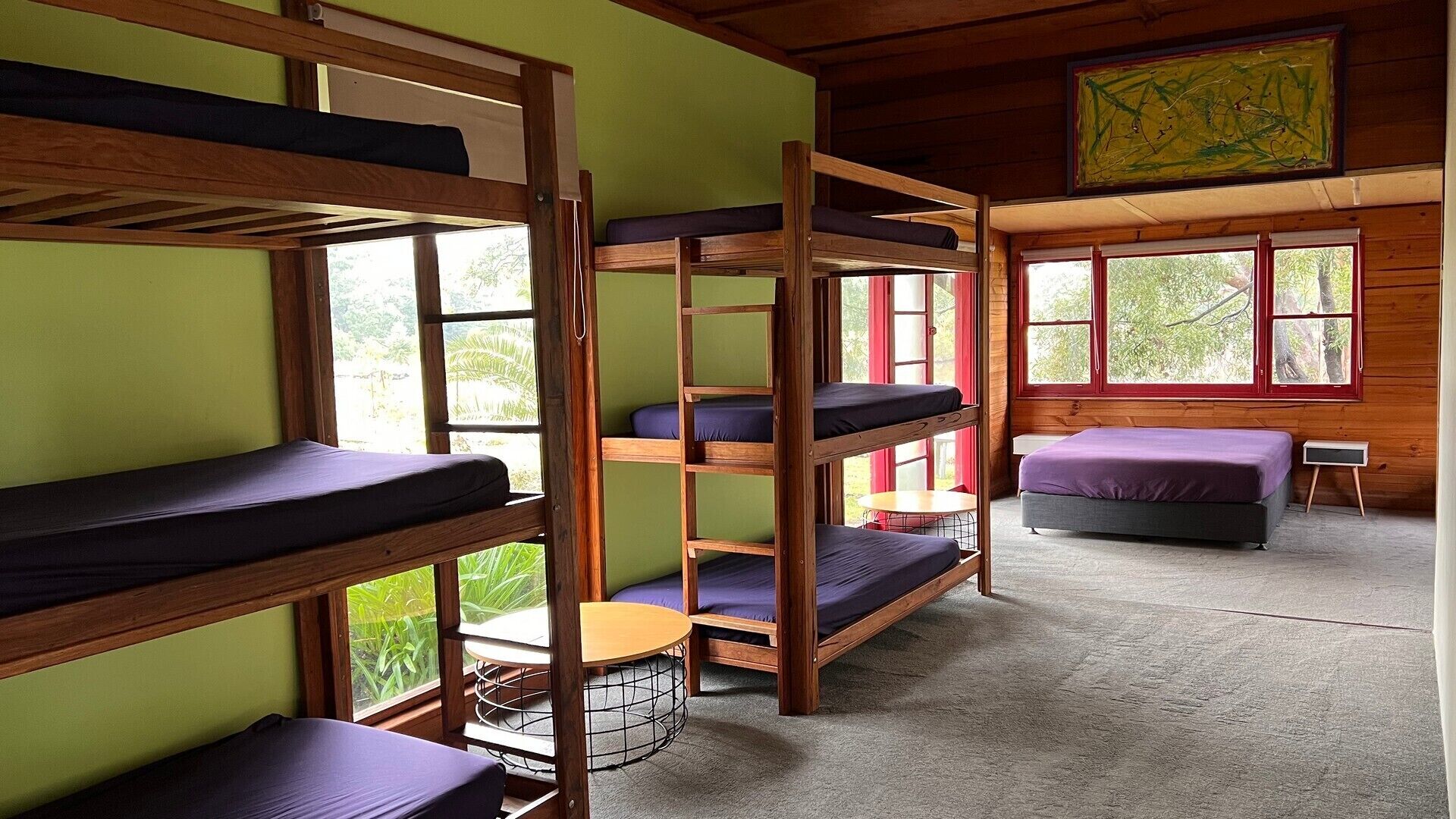 A dormitory room with bunk beds, a small round table, and a window with a view of greenery.