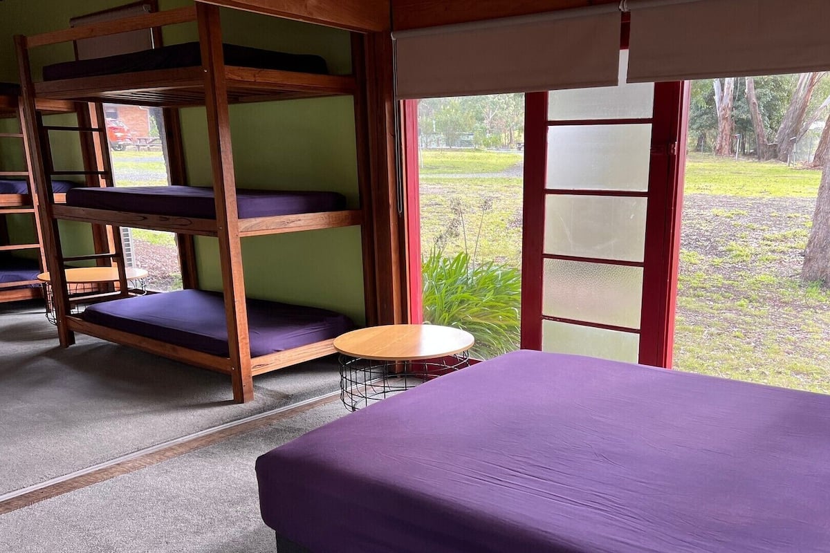 Una habitación con literas, una mesa redonda y una ventana con vistas a zonas verdes.
