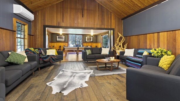 A spacious living room with a wooden ceiling, a large sofa set, a coffee table, and a rug. - Mingling Waters (Nowa Nowa)
