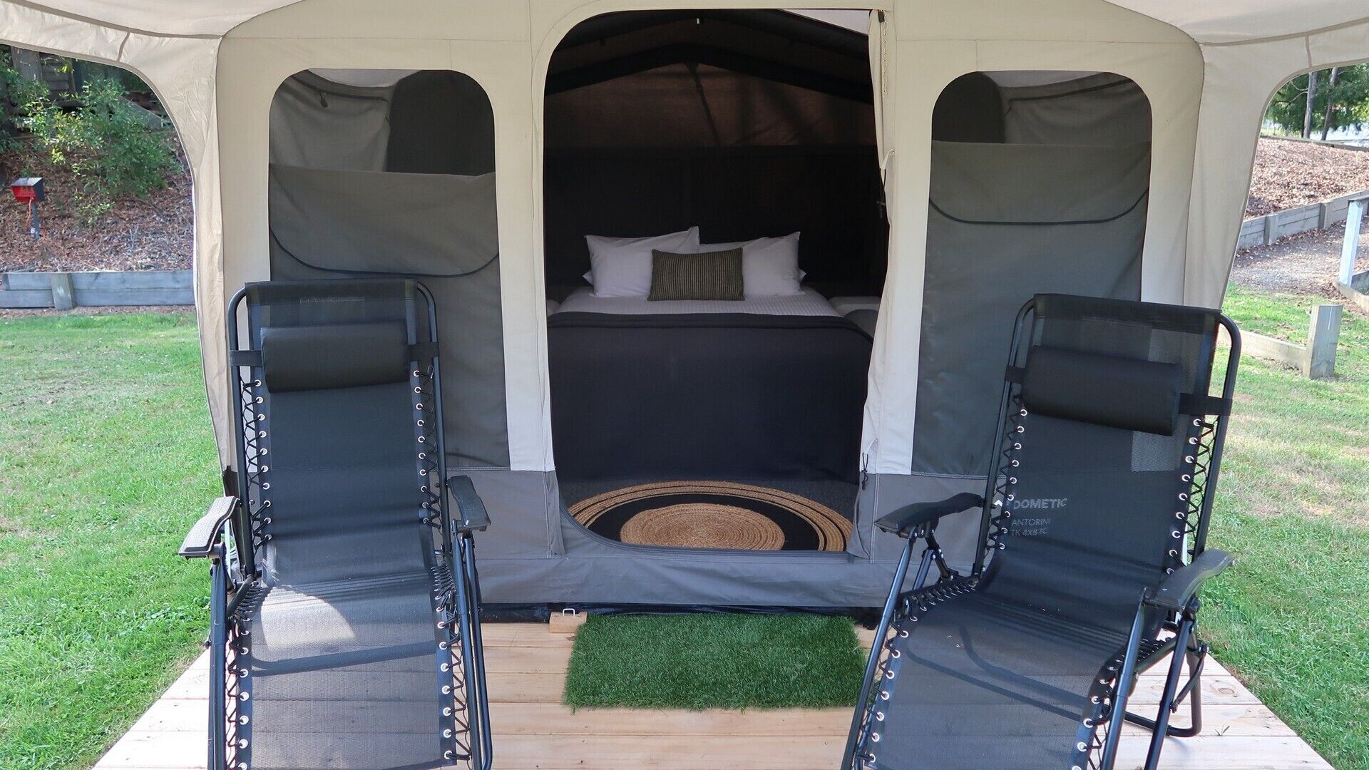 A tented outdoor sleeping area with a bed, two reclining chairs, and a small rug.