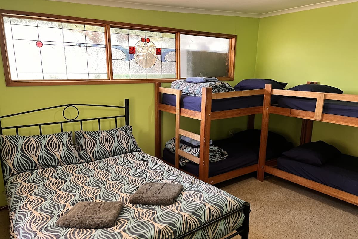 Una habitación con una cama litera, una cama individual con ropa de cama estampada y un ventanal con un diseño de vitral.
