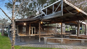 A rustic wooden cabin with a covered patio area, benches, and string lights. - Mingling Waters (Nowa Nowa)
