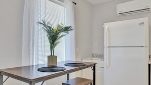 A small kitchen with a white refrigerator, a window with white blinds, and a potted plant on the counter.