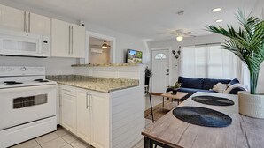 A modern kitchen with white cabinetry, a built-in microwave, and a stove. There is a dining area with a wooden table and blue sofa.