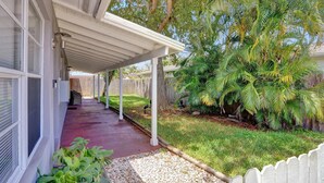 A covered porch with a view of a backyard, a wooden fence, and various plants.