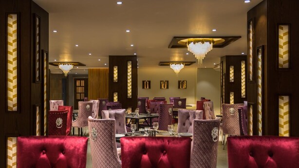 A formal dining area with velvet chairs, chandeliers, and framed artwork on the walls. - Oasis Hotel Cumilla (Comilla)