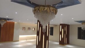 A spacious room with a large chandelier, wooden columns with illuminated panels, and a wooden door. - Oasis Hotel Cumilla (Comilla)