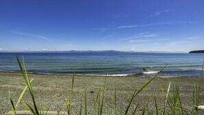 Ein Kiesstrand mit klarem, blauem Wasser und Bergen im Hintergrund.