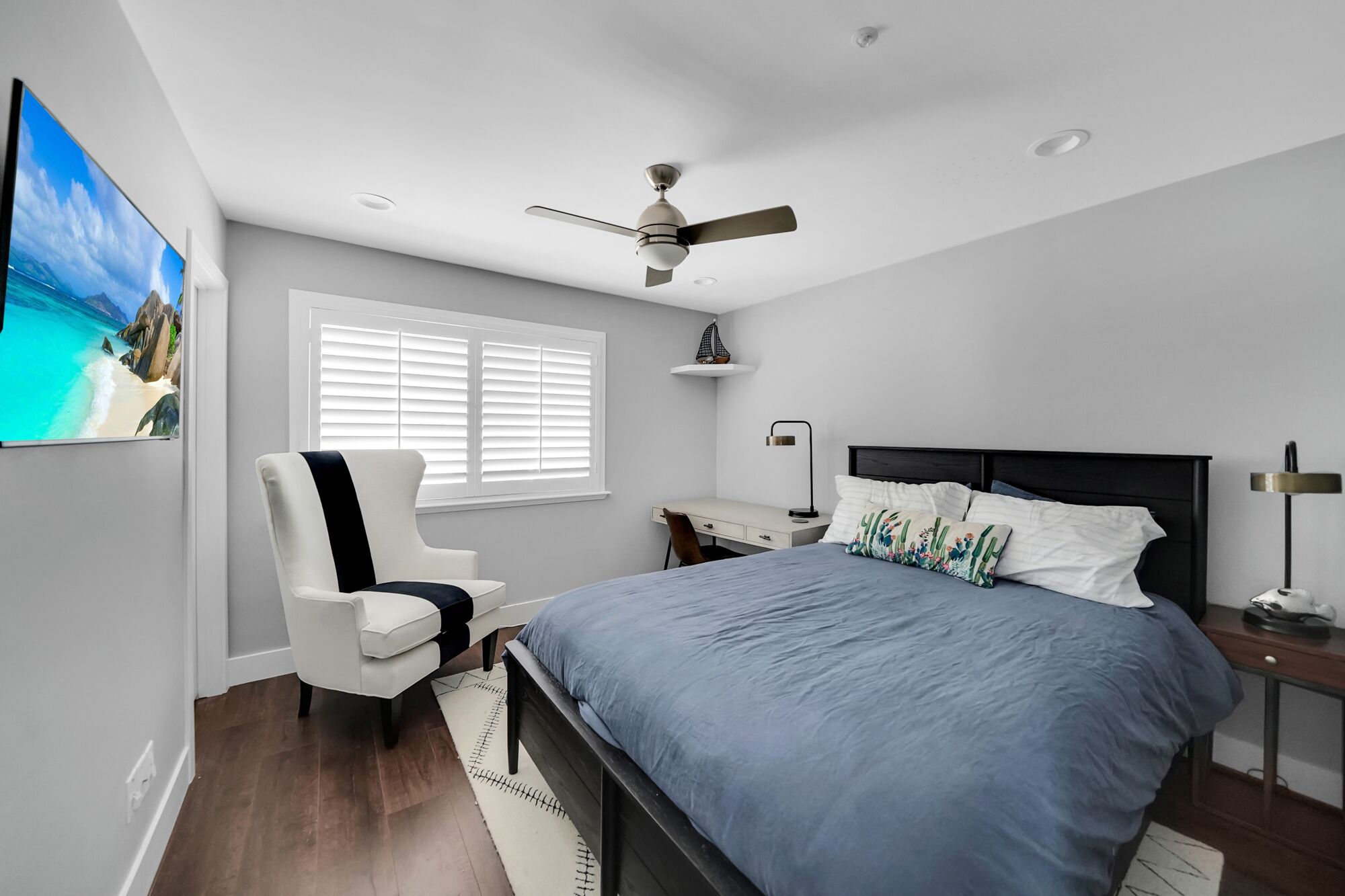 Un dormitorio con cama, escritorio, silla, ventilador de techo y ventana con persianas.