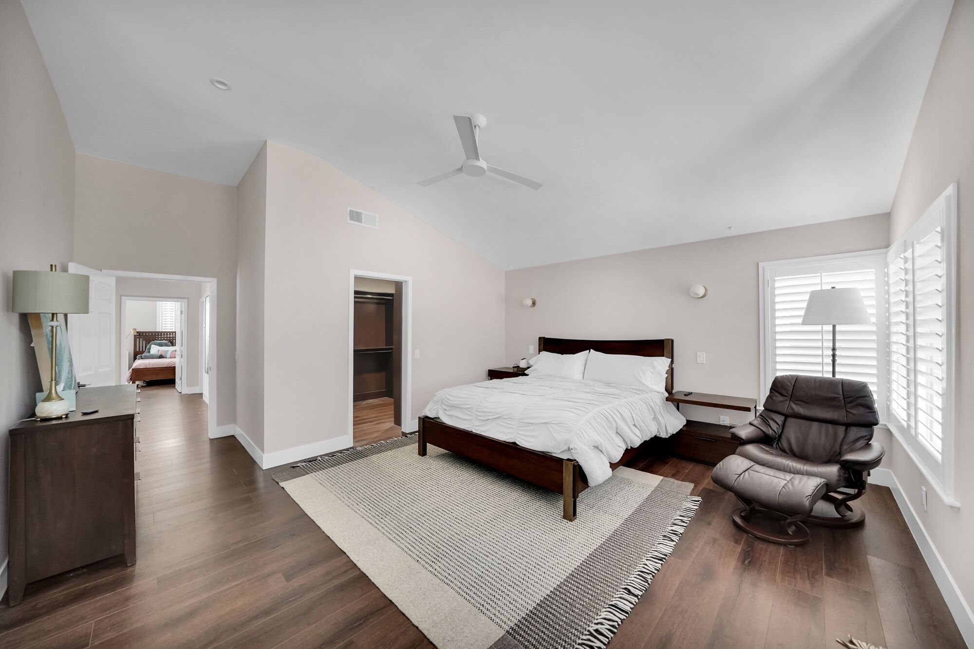 A spacious bedroom with a large bed, a ceiling fan, a walk-in closet, and a window with blinds.