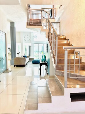 Ein geräumiger Wohnbereich mit moderner Treppe, einer großen Uhr und Blick ins Freie.