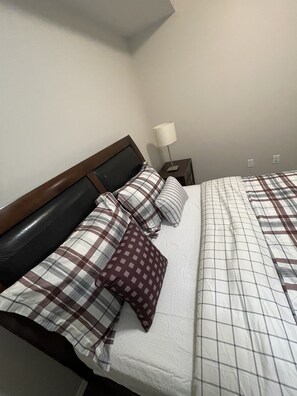 Un lit bien fait, avec une couverture à carreaux et plusieurs oreillers, dont un à motifs.