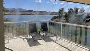 A balcony with two chairs overlooking a lake, with mountains in the background and a house to the right.