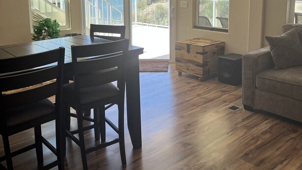 A spacious living area with a dining table, chairs, a sofa, and a view of a lake through large windows.