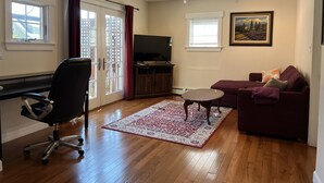 Un salon avec un téléviseur, un canapé, un fauteuil, un tapis et un tableau accroché au mur.