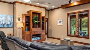 Een ruime woonkamer met een leren bank, een houten mediameubel en een groot raam met uitzicht op de omgeving.
