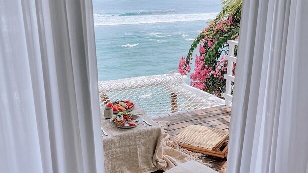 Um deck de madeira com uma mesa posta para refeições, com vista para o oceano.