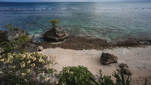 Paisagem costeira com águas cristalinas, praia arenosa e afloramentos rochosos.