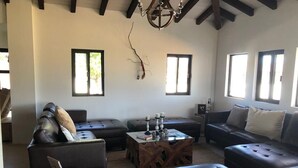 Ein geräumiges Wohnzimmer mit hoher Decke, dunklen Ledersofas, einem Couchtisch und großen Fenstern, die für natürliches Licht sorgen.