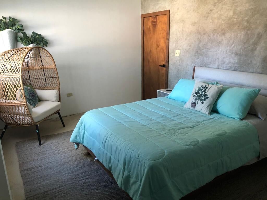 Une chambre à coucher avec un lit, une chaise en osier, une porte en bois et une plante en pot.