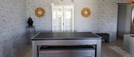 Una habitación con una mesa grande, dos apliques de pared, un armario blanco y dos coronas en la pared.