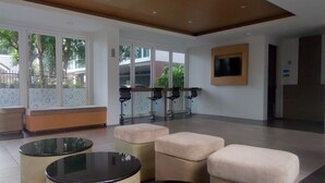A modern lobby with a seating area, a TV mounted on the wall, and large windows providing natural light. - Kata Beach Ozone Superb Fully Equipped Studio Kitchen Washing Machine air con (Karon)