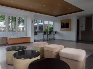A modern lobby with a seating area, a TV mounted on the wall, and large windows providing natural light.
