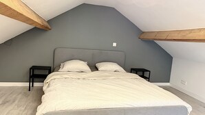 A bedroom with a sloped ceiling, a grey headboard, two bedside tables, and a bed with a patterned bedspread. - House With Free Parking 15min From The Airport (Charleroi)