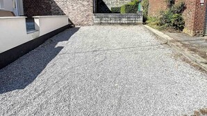 A residential area with a gravel driveway, brick walls, and a modern building with a sloped roof. - House With Free Parking 15min From The Airport (Charleroi)