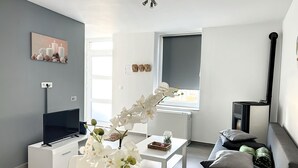 A modern living room with a flat-screen TV, a white coffee table, a sofa, and a window with a view. - House With Free Parking 15min From The Airport (Charleroi)