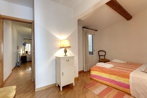 Une chambre à coucher avec un lit, une table de chevet, une lampe, une chaise et une fenêtre avec des rideaux.