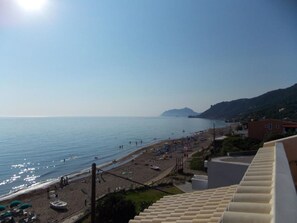 Blick auf die Küste mit Strand, blauem Himmel und Bergen in der Ferne.