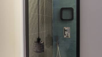 A modern bathroom with a glass shower enclosure, a handheld showerhead, and a control panel.