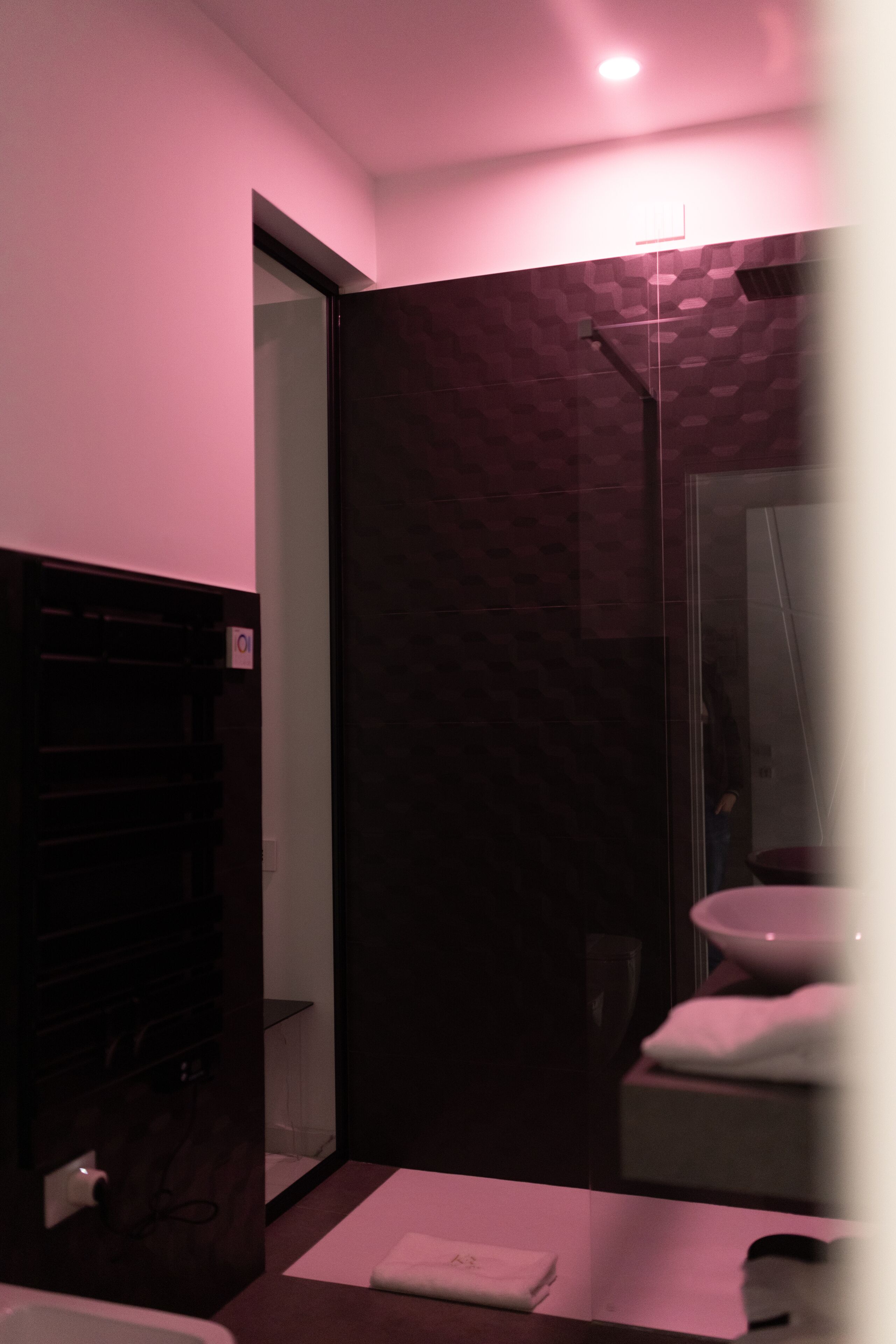 A modern bathroom with a dark marble wall, a glass shower enclosure, and a white sink.