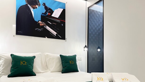 A hotel room with a bed, green and white pillows, a painting of a man playing the piano, and a door with a geometric pattern. - Room in B&B - B&B Kreart Suite & Rooms (Crotone)