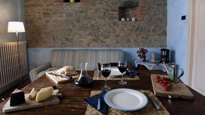 Un coin repas avec un mur en pierre, un canapé, une table dressée avec de la nourriture, des verres à vin et une machine à café.