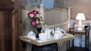 Un plateau en bois avec des tasses à thé blanches, une théière et un vase rempli de fleurs, dans une pièce dont le mur est en briques et qui contient un lit en bois.