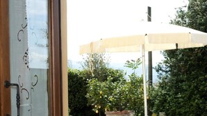 Une porte en bois avec un panneau de verre, une table ornée d’un vase de fleurs roses et un espace extérieur aménagé avec une table, des chaises et un parasol blanc.