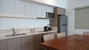 A modern kitchen with a wooden dining table, a built-in microwave, and a refrigerator. - One Bedroom, Great Location Steps From the Beachh, Beautiful Roof Top View! (Playa del Carmen)