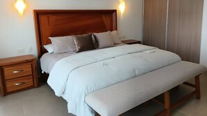 A neatly made bed with a wooden headboard, two bedside tables, and a bench at the foot of the bed. - One Bedroom, Great Location Steps From the Beachh, Beautiful Roof Top View! (Playa del Carmen)