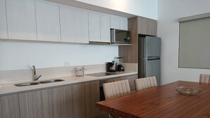 A modern kitchen with a wooden dining table, white cabinets, and a built-in microwave. - One Bedroom, Great Location Steps From the Beachh, Beautiful Roof Top View! (Playa del Carmen)