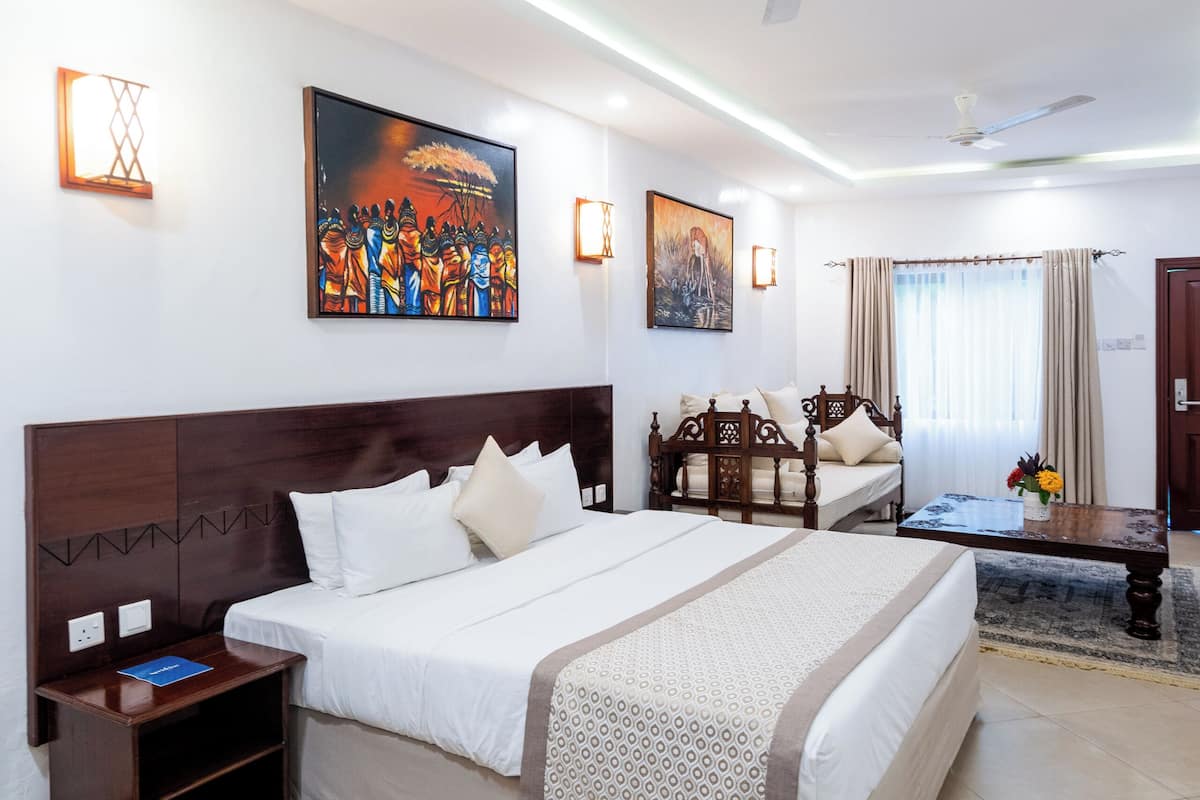 A hotel room with a large bed, a wooden headboard, a nightstand, a desk, a ceiling fan, and artwork on the walls.