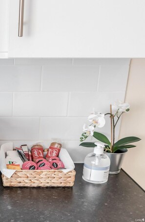 En köksbänk med en flätad korg som innehåller olika förpackade varor, en flaska handsprit och en orkidé i en kruka.