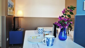 A hotel room with a dining table set with plates, a blue mug, a vase with purple flowers, a lamp, and a blue cabinet. - La Bouganville Studio 200 m From the sea (Sperlonga)