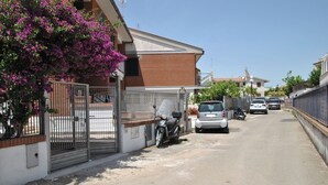 A residential street with parked cars and a motorcycle, a gated entrance, and a building with a brick facade. - La Bouganville Studio 200 m From the sea (Sperlonga)